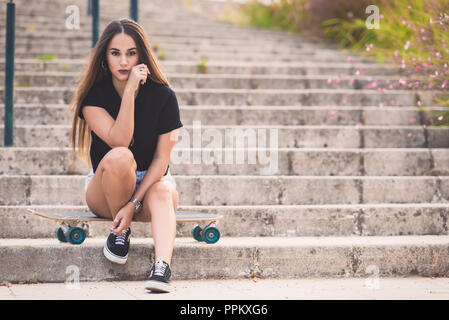 Schöne junge Frau sitzt auf Skateboard Stockfoto