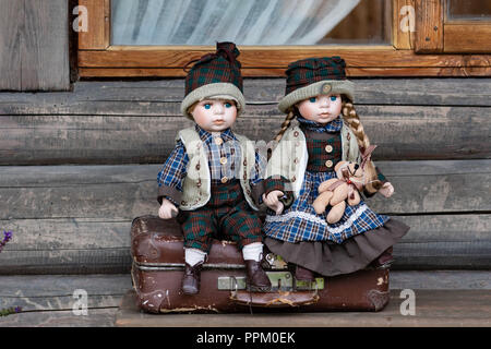 Antike porzellan Puppen sitzt auf Koffer in der Nähe von Bauernhaus anmelden. Stockfoto