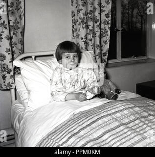 1950, historische, ein junges Mädchen in einem Krankenhausbett sitzen mit einem Stofftier, ihr Teddy Bär neben ihr, England, UK. Stockfoto