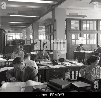 1950, historische, männliche und weibliche Angestellte am Schreibtisch sitzen in einem Büro, England, UK. Stockfoto
