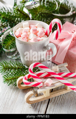 Weiß und rosa Marshmallows in eine Schale, Weihnachten Zuckerstangen und Spielzeug Schlitten auf einem weißen Tisch. Thema Weihnachten. Stockfoto