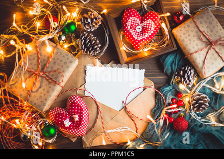 Weihnachten und Neujahr Hintergrund mit Geschenkboxen mit Beleuchtung, dekorative Herzen, Kegel und Umschlag mit Grußkarte Stockfoto