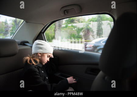 Traurig einsam wenig schönes Mädchen in Hut und Mantel sitzen im Auto in der Nähe der Fenster Stockfoto