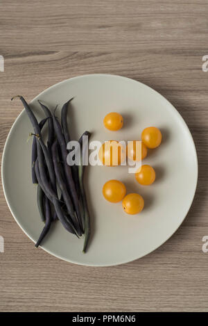 Ansicht von oben Purpur grüne Bohnen und Gelbe Kirschtomaten auf einer Platte Stockfoto