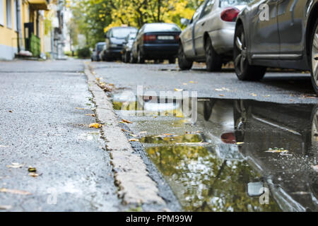 Autos in der Nähe der Wohngebäude geparkt. Wasser Pfützen auf Asphaltstraße nach regen Stockfoto