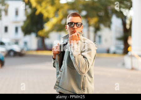 Junge schöne modische Mann in eleganter Kleidung Denim mit Brille in der Stadt Stockfoto