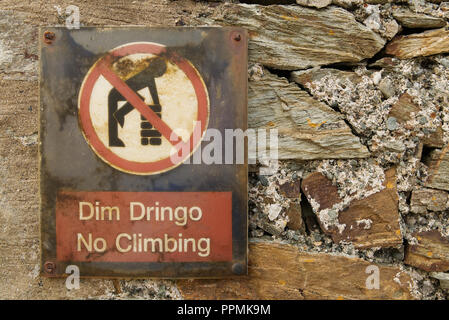 Die walisische Sprache keine Klettern Dim Dringo Zeichen auf einer alten Steinmauer mit Symbol des Menschen Klettern an einer Wand in einem roten Kreis mit roten Linie durch Stockfoto