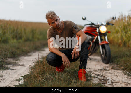 Stilvolle hübscher junger Mann in einem Green Fashion T-Shirt sitzen ist in der Nähe ein Fahrrad in einem Maisfeld. Einsame Reisende auf dem Fahrrad Stockfoto