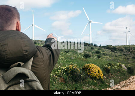 Ein Tourist mit einem Rucksack neben Windmühlen in Portugal. Er weist mit der Hand auf die Distanz. Stockfoto