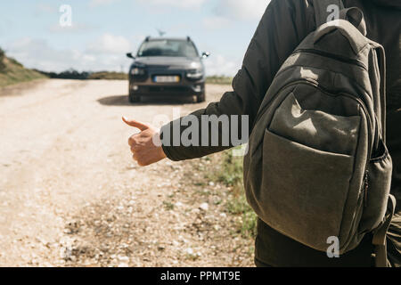 Nahaufnahme eines Mannes Wanderer mit Rucksack trampen. Er hob den Finger auf und versucht, das Auto seine Reise fortsetzen zu stoppen. Stockfoto