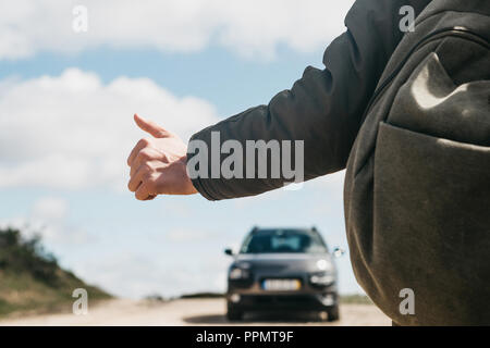 Nahaufnahme eines Mannes Wanderer mit Rucksack trampen. Er hob den Finger auf und versucht, das Auto seine Reise fortsetzen zu stoppen. Stockfoto
