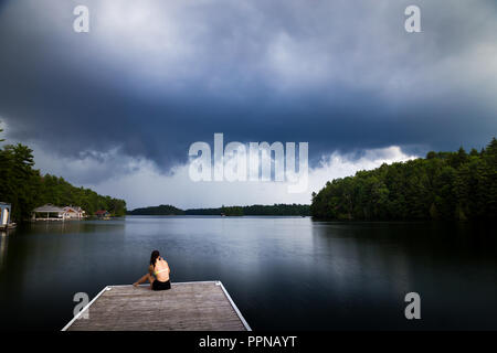 Junge brünette Frau sitzt auf einem Dock an einem See in einem Sturm kommen. Stockfoto