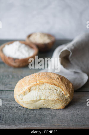 Frische Handwerk Brot bedeckt mit grau Leinen Servietten liegen auf dem Hintergrund der alten hölzernen Brettern. Bild vertikal mit copy-Raum Stockfoto