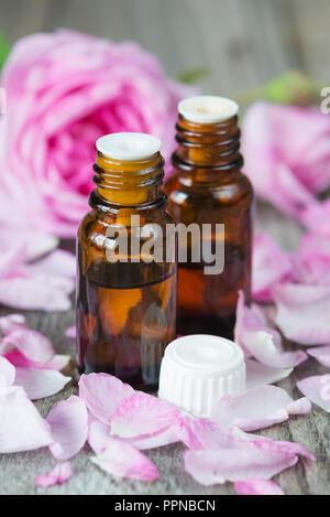 Zwei dunkle Durchstechflaschen mit Rose ätherisches Öl und Rosen auf einem hölzernen Hintergrund Stockfoto