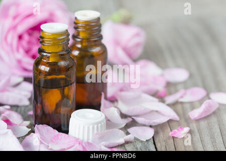 Zwei dunkle Durchstechflaschen mit Rose ätherisches Öl und Rosen auf einem hölzernen Hintergrund mit copy-Raum Stockfoto