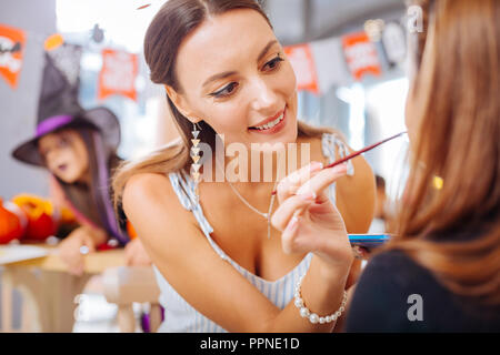 Schöne Frau tragen Zubehör Malerei Gesicht des kleinen Mädchens für Halloween Stockfoto