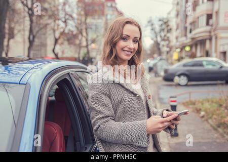 Glückliche Frau mit Handy stand neben ihr Auto Stockfoto