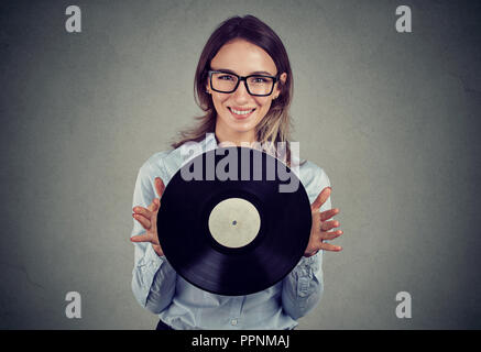 Junge Frau in Gläser holding Vintage vinyl Record an Kamera lächeln Stockfoto