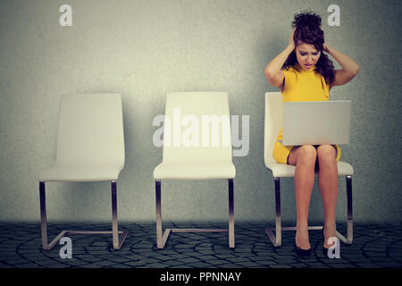Junge stilvolle Frau in Stress zu quetschen Kopf sitzend auf Stuhl, während mit Laptop Stockfoto