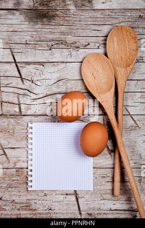 Eier, Löffel und leeres Papier auf rustikalen Holztisch Stockfoto