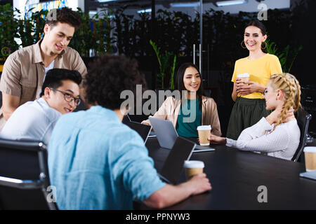 Interracial Geschäftspartner mit Papier Tassen Kaffee in Sitzung am Tisch mit Laptops in modernen Büro Stockfoto