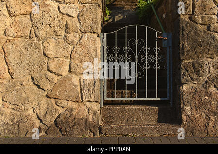 Gelbes Feld Steinmauer beleuchtet durch die Abendsonne mit schmiedeeiserne Tor, die eine Treppe nach oben in den Garten führende öffnet Stockfoto