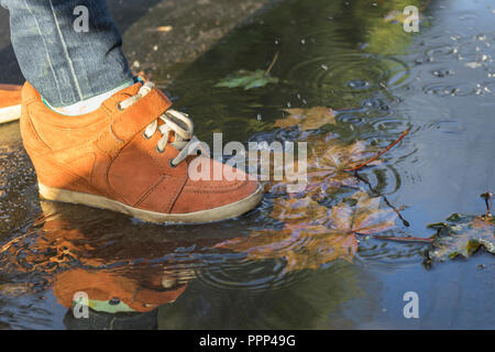 Frau Fuß zu Fuß in einer Pfütze in der orange Stiefel. Stockfoto