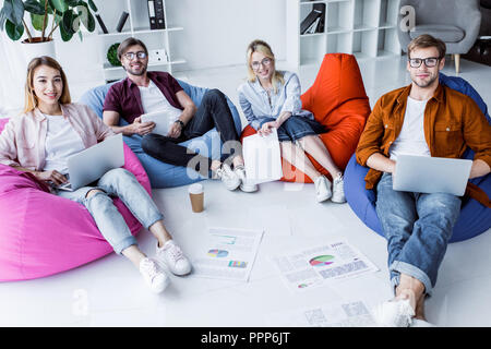 Multikulturelle Kollegen arbeiten an Startprojekt in Büro- und sitzen auf Sitzsäcken mit Gadgets Stockfoto