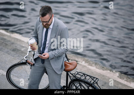 Geschäftsmann mit Kaffee trinken gehen und Smartphone mit Fahrrad am Kai Stockfoto