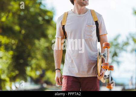 Teilansicht der Mann mit Rucksack und Longboard gehen auf die Straße Stockfoto