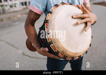 7/8-Ansicht der afrikanischen amerikanischen Straßenmusiker Djembe spielen in Stadt Stockfoto