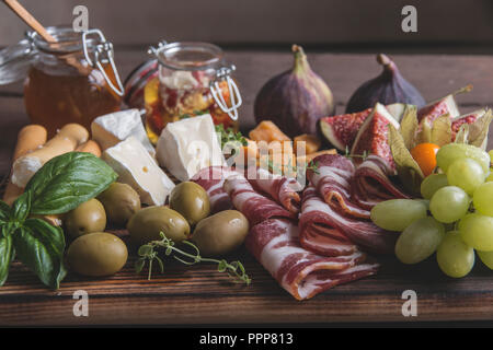 Prosciutto, Camembert, Feigen, Honig, Trauben, Oliven auf dunklen, das Brett über rustikal Hintergrund Stockfoto