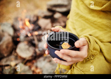 Tasse heißen Tee in der Frau die Hand ist der Herbst in einem Wald in Goldgelbe Laub. Der Herbst kam, magische Stimmung. Gelbe Blätter schweben im Kaffee Stockfoto