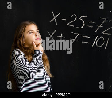 Ein kleines Mädchen steht in der Nähe einer Schule und versucht, eine schwierige Aufgabe für Sie in Mathematik zu lösen Stockfoto