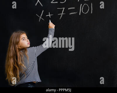 Ein kleines Mädchen steht in der Nähe einer Schule und versucht, eine schwierige Aufgabe für Sie in Mathematik zu lösen Stockfoto