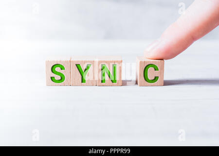 Das Wort Sync gebildet durch Holzblöcke und arrangiert von einem männlichen Finger auf einem weißen Tisch Stockfoto