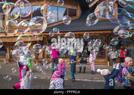 Karpacz, Polen - Februar 2018: Kinder, die versuchen, riesige Seifenblasen auf der Hauptstraße in Karpacz Stadt zu fangen, polnische Winter Skigebiet Stockfoto