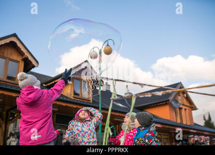 Karpacz, Polen - Februar 2018: Kinder, die versuchen, riesige Seifenblasen auf der Hauptstraße in Karpacz Stadt zu fangen, polnische Winter Skigebiet Stockfoto