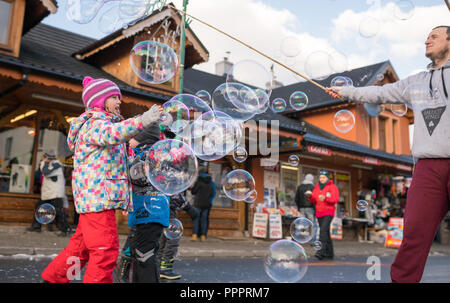 Karpacz, Polen - Februar 2018: Kinder, die versuchen, riesige Seifenblasen auf der Hauptstraße in Karpacz Stadt zu fangen, polnische Winter Skigebiet Stockfoto