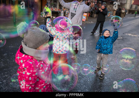 Karpacz, Polen - Februar 2018: Kinder, die versuchen, riesige Seifenblasen auf der Hauptstraße in Karpacz Stadt zu fangen, polnische Winter Skigebiet Stockfoto