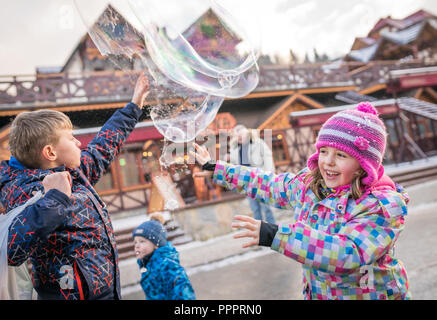 Karpacz, Polen - Februar 2018: Kinder, die versuchen, riesige Seifenblasen auf der Hauptstraße in Karpacz Stadt zu fangen, polnische Winter Skigebiet Stockfoto