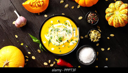 Von oben Blick auf Kürbissuppe mit Kräutern und Gemüse und Samen auf hölzernen Hintergrund umgeben Stockfoto