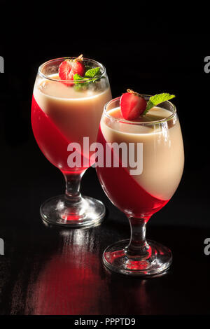 Cherry und milchpudding in die Gläser mit Minze und Erdbeere Stücke auf dem schwarzen Hintergrund Stockfoto