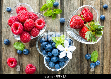 Mischung aus frischen Beeren in ein Glas-Förmchen in Form von Herzen, auf hölzernen Hintergrund, Ansicht von oben Stockfoto