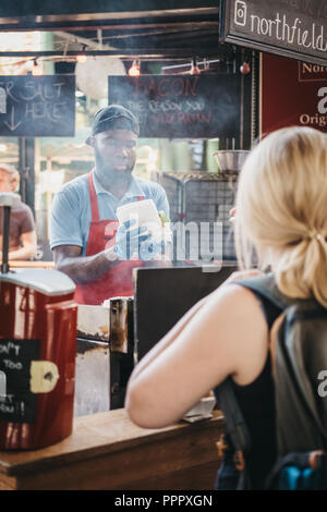 London, UK - 17. September 2018: Frau wartet auf ihr Essen in Northfield Metzgerei stand in Borough Markt, Personal kochen im Hintergrund. Borough M Stockfoto