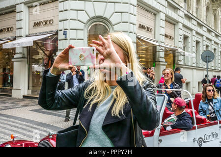 Junge Frau, die am Telefon vor dem Luxusgeschäft Jimmy Choo in der Parizska Straße, Prag, Tschechische Republik fotografiert Stockfoto