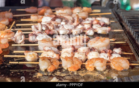 Grillen Meeresfrüchte, Shrimps, Calamares auf dem Grill. Die Metallplatte des Grill mit Blick auf das Meer essen Fleisch, Garnelen, Tintenfisch. Stockfoto