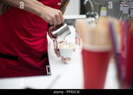 Barista gießt Kaffee in eine Tasse und schafft eine schöne Bild aus Schaumstoff. Close Up. Hände Stockfoto