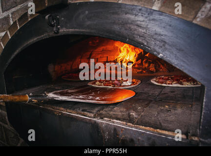 Professionelle Pizzaofen. Ein gutes Feuer brennt im Ofen. Drei Pizzas in den Ofen. Kochen Pizza im Cafe. Stockfoto
