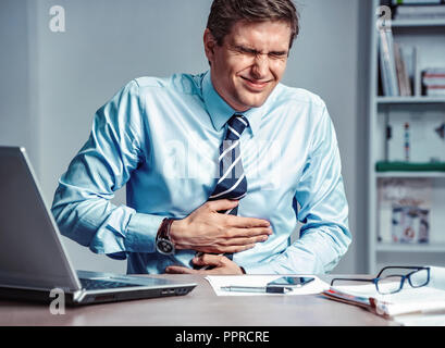 Mitarbeiter leidet unter starken Schmerzen im Magen. Foto der Mann bei der Arbeit im Büro. Medizinisches Konzept. Stockfoto